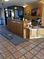 Un espace d’accueil avec un comptoir en bois, le logo de Days Inn sur le tapis d’entrée, une horloge et un tableau représentant une formation rocheuse.
