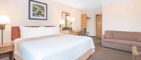 A hotel room with a large bed, a desk, a chair, a sofa, and a mirror.