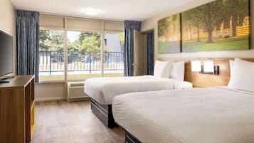 A hotel room with two beds, a TV, a large window with curtains, and a painting on the wall.