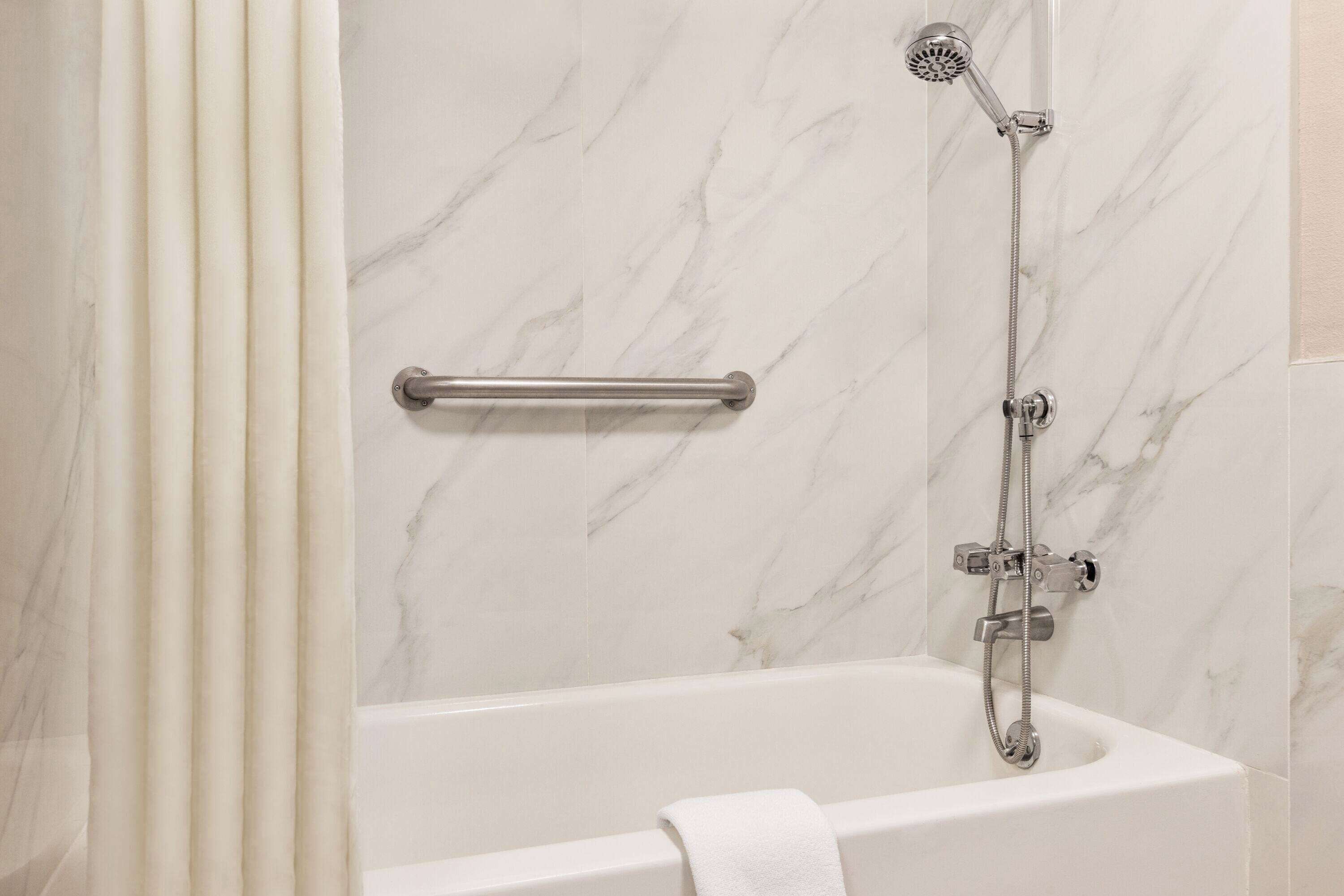 A bathroom with a white bathtub, a handheld showerhead, and a grab bar.