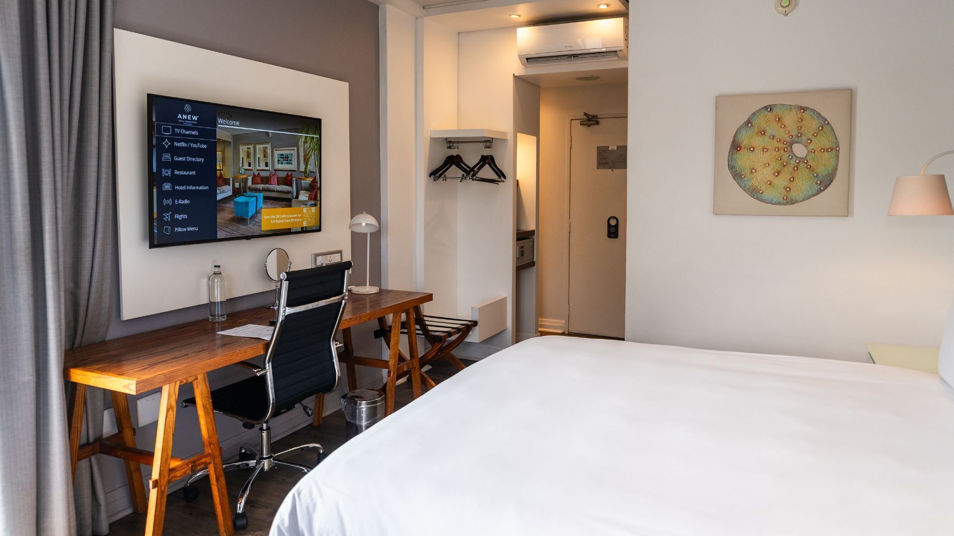 Habitación de hotel con cama, escritorio, silla, televisor y obras de arte.