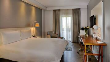 Habitación de hotel con una cama grande, un escritorio con silla, un televisor y una ventana con cortinas.
