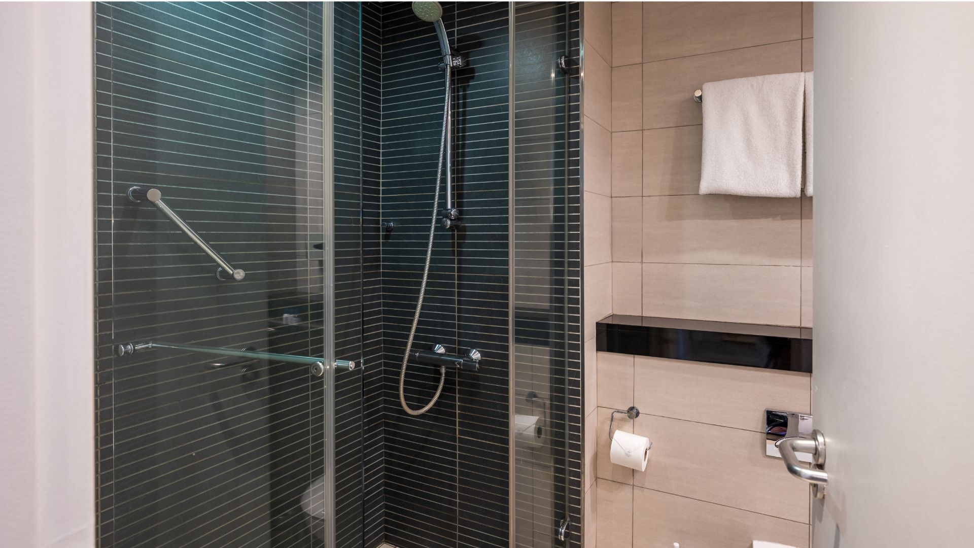 Un baño moderno con cabina de ducha de vidrio, un perchero para toallas y un dispensador de papel higiénico.