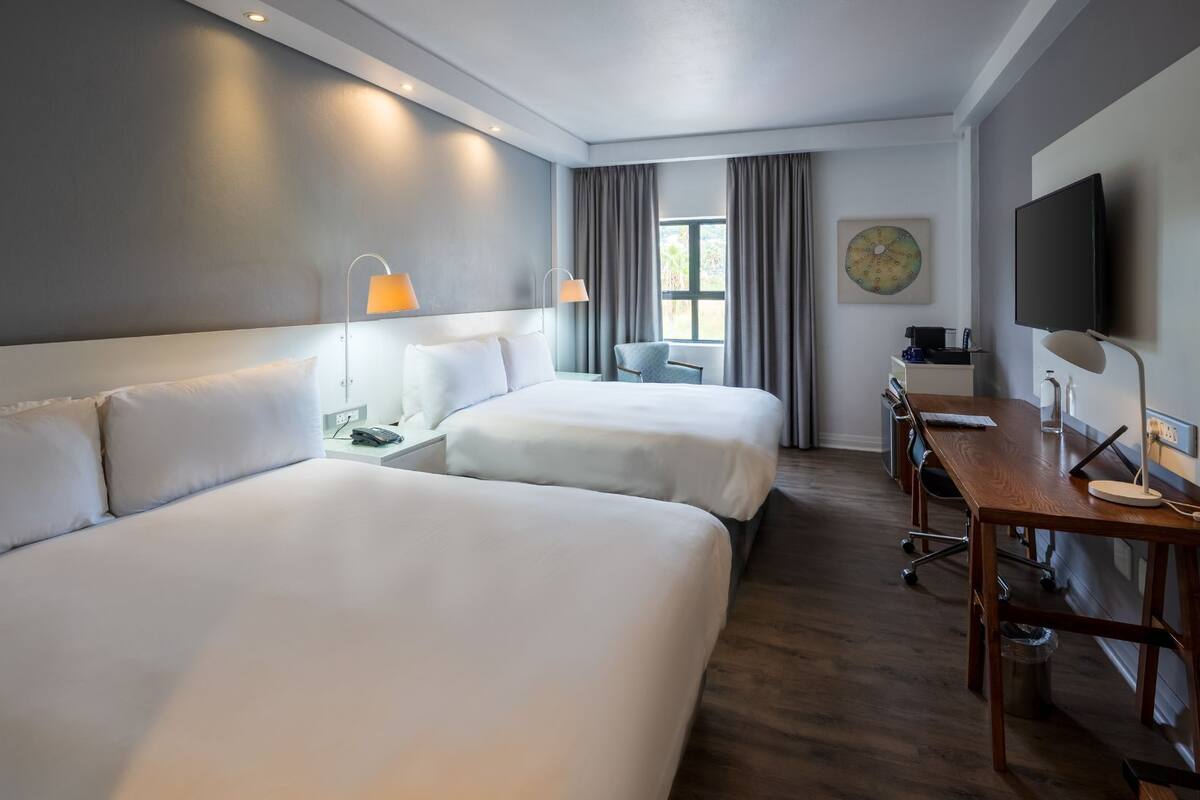 Une chambre d’hôtel avec deux lits, un bureau, une télévision et une fenêtre avec des rideaux.