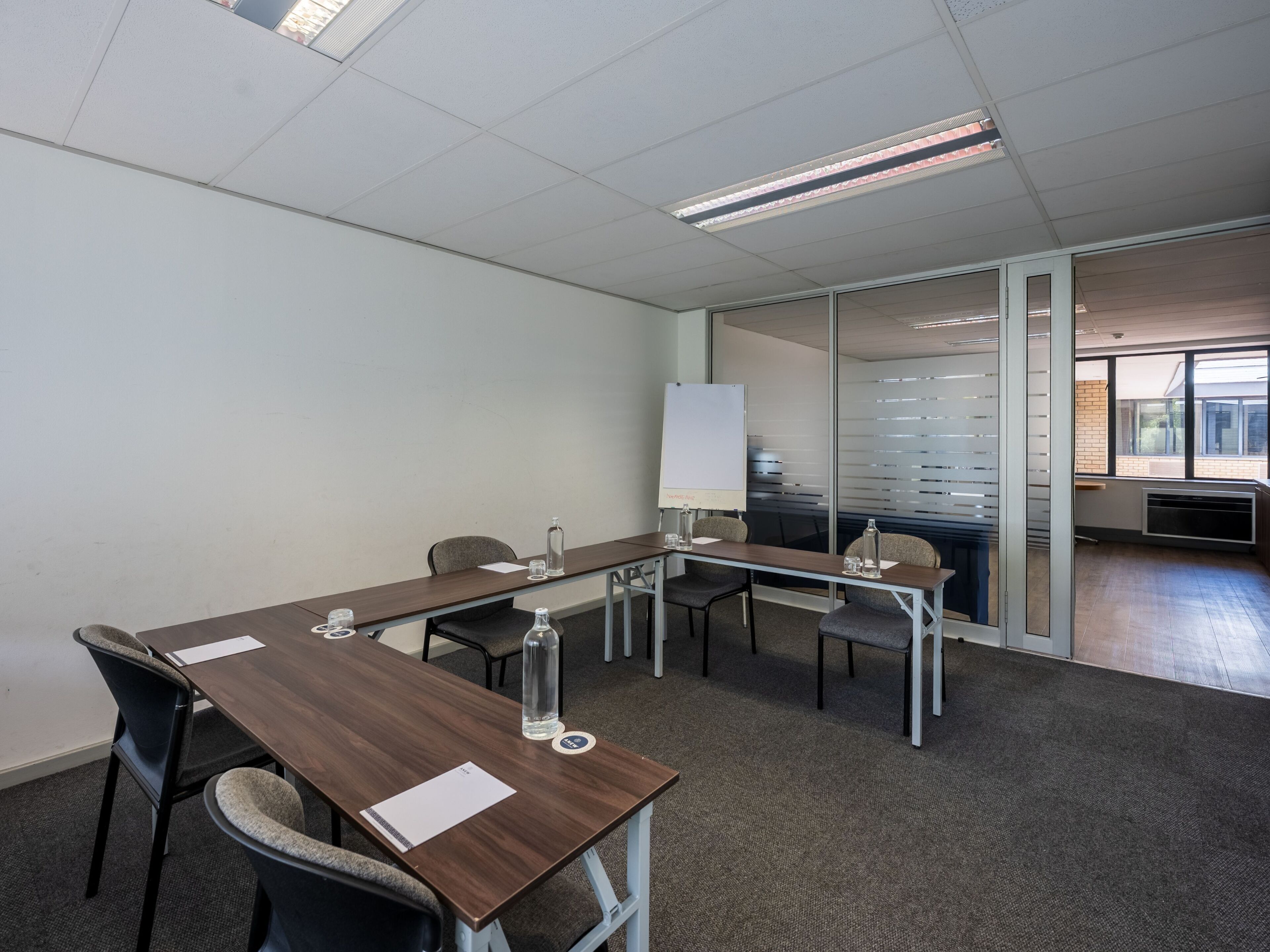 A conference room with a long table, chairs, a whiteboard, and a glass partition.