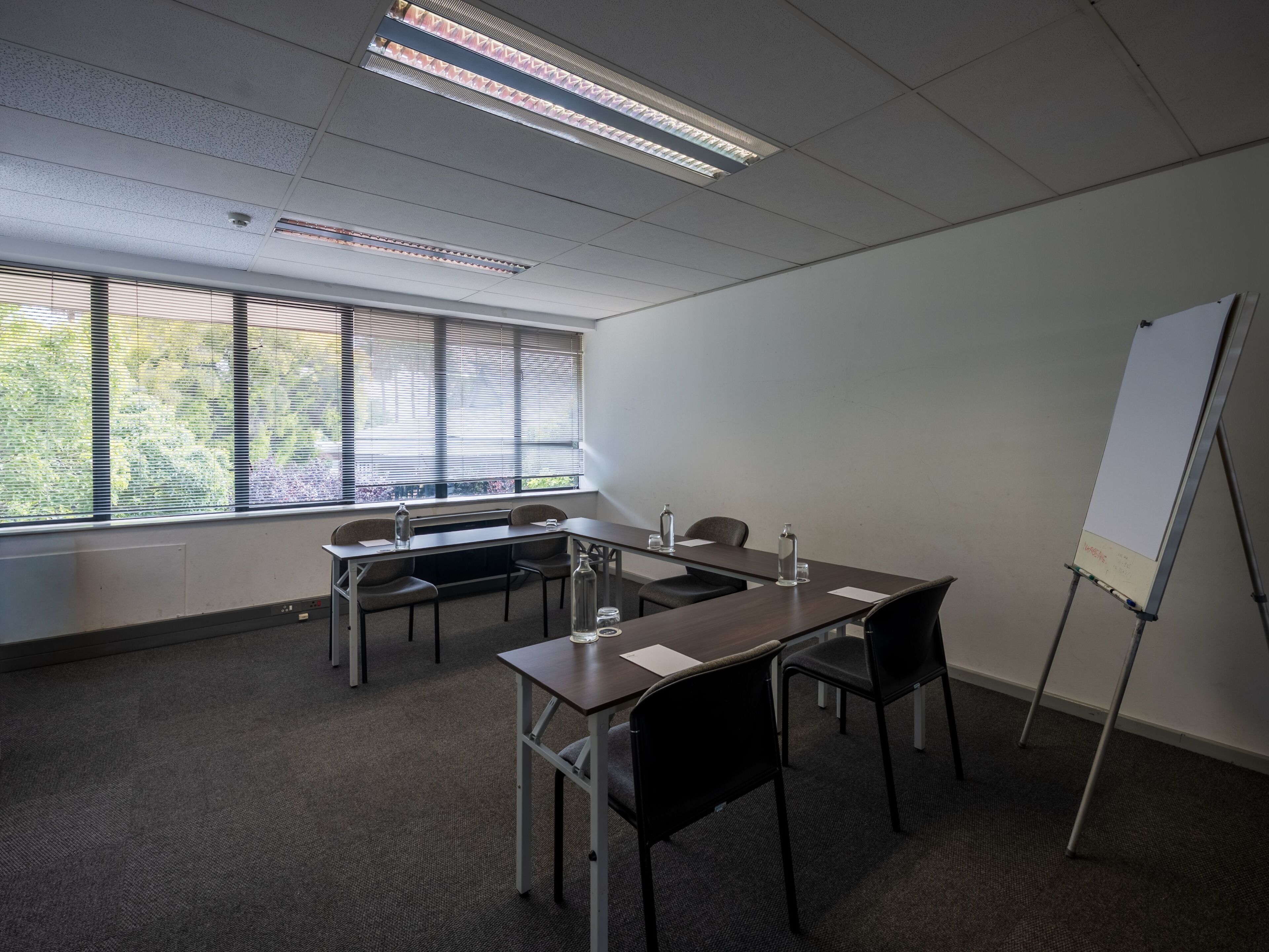 A conference room with a long table, chairs, a whiteboard, and large windows with blinds.