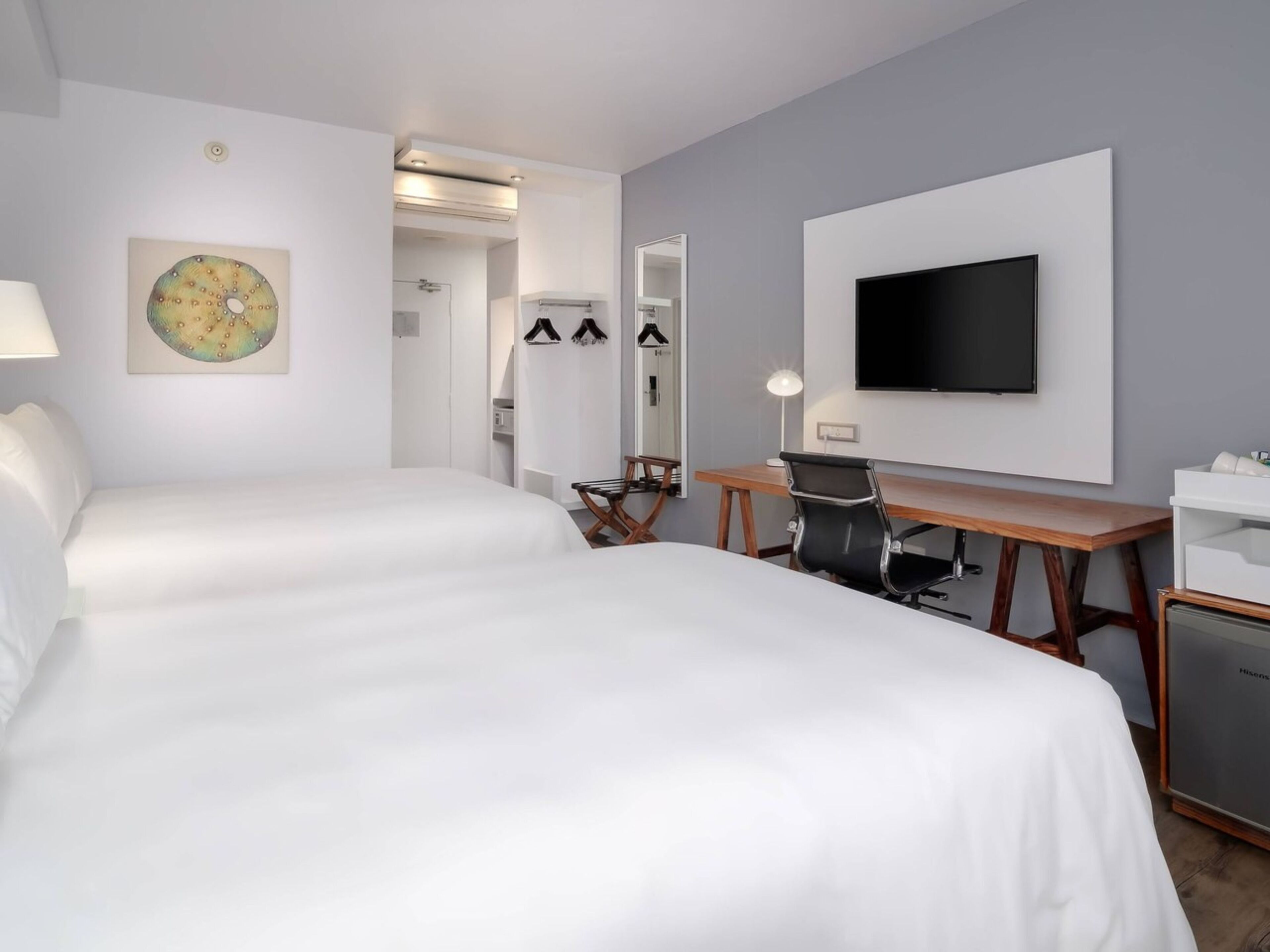 A hotel room with two beds, a desk, a chair, a TV, and a mirror.