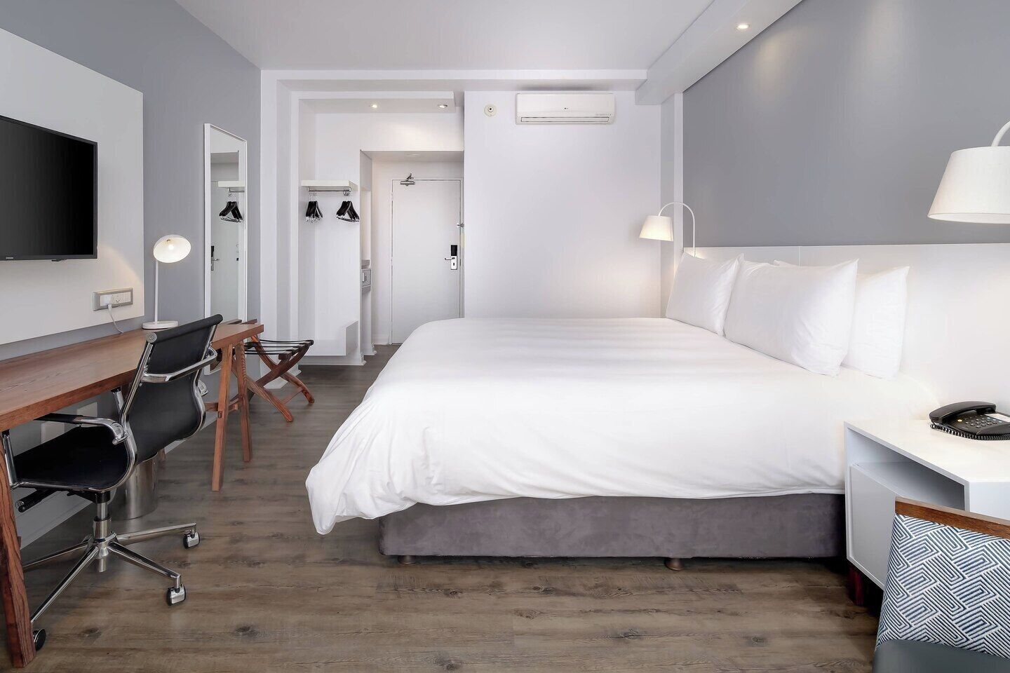 Een moderne hotelkamer met een groot bed, een bureau met stoel, een televisie en een kledingkast.
