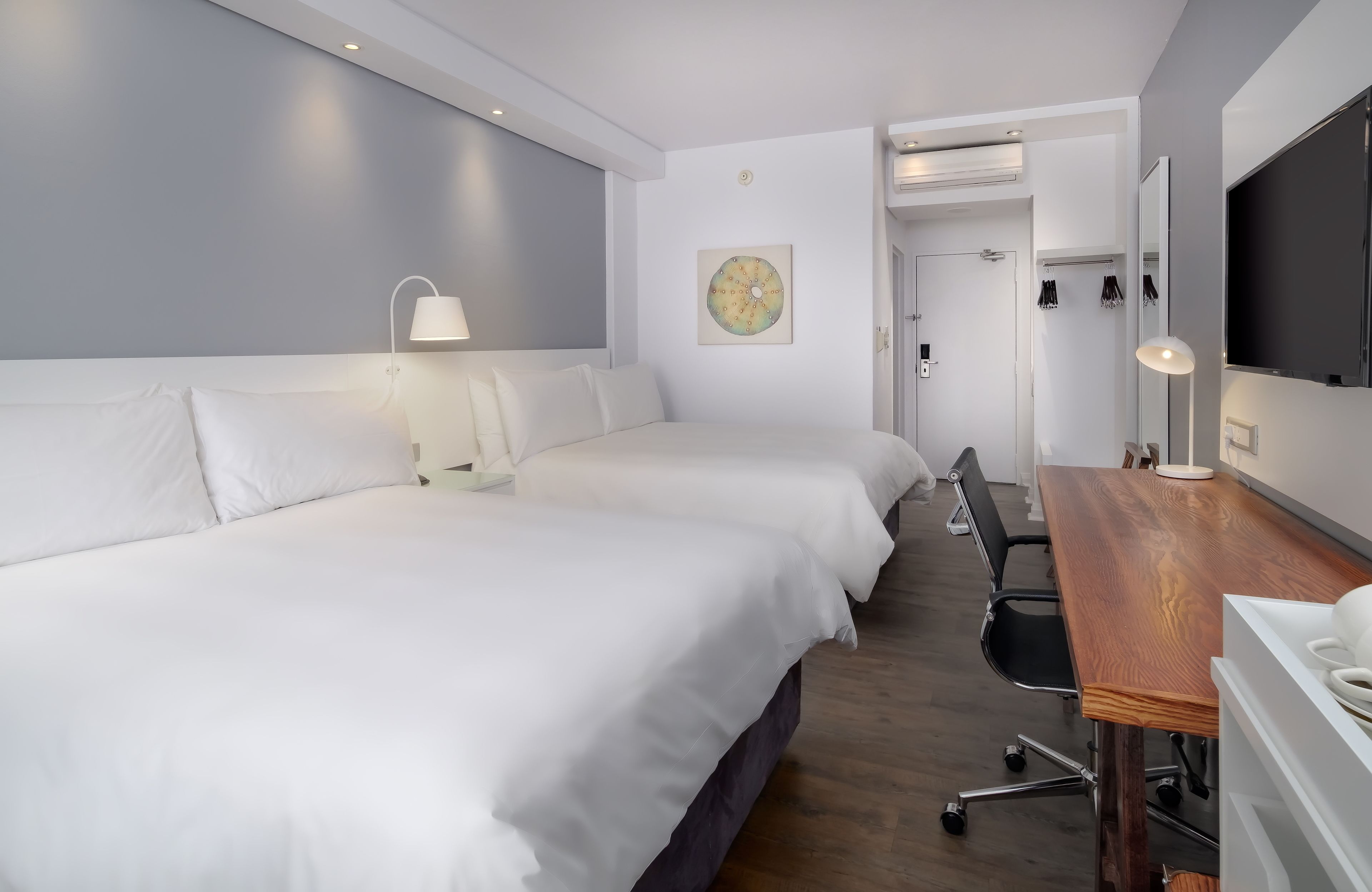 Habitació d'hotel amb dos llits, una taula de fusta, una cadira, una làmpada de taula, un televisor fixat a la paret i una porta que dona a un bany.