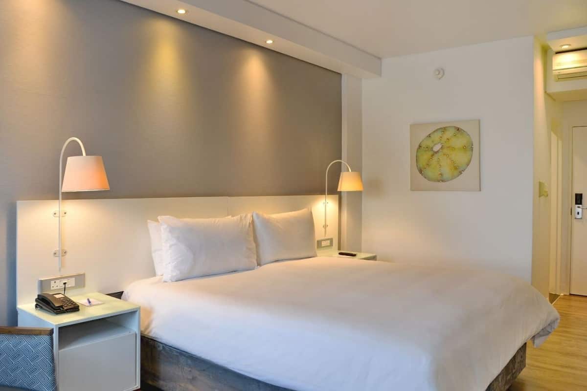 Une chambre d’hôtel moderne dotée d’un grand lit, de deux tables de chevet avec des lampes, d’un petit coin salon et d’une porte donnant accès à la salle de bain.