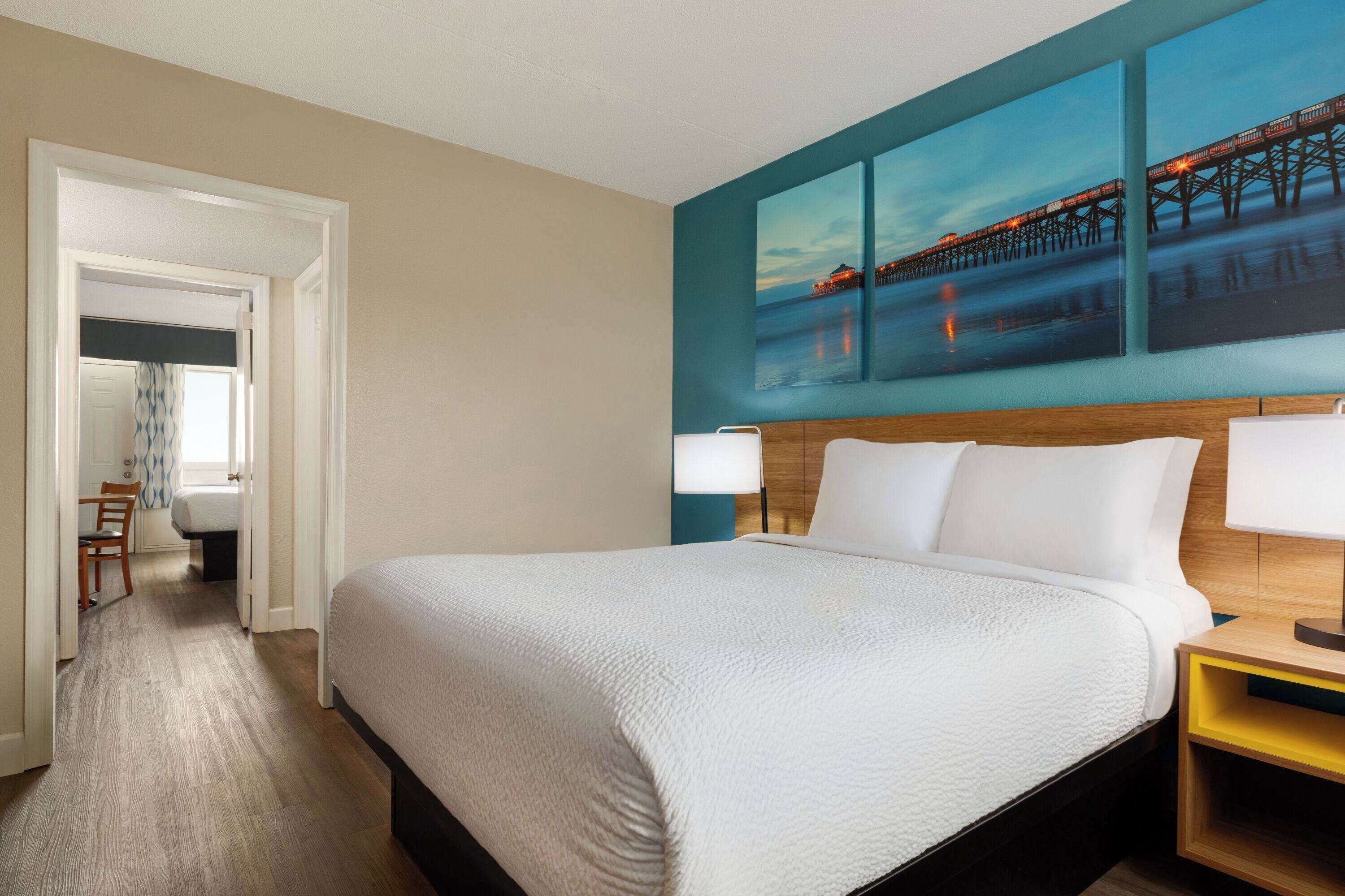 A hotel room with a large bed, a wooden headboard, and a painting of a pier on the wall.