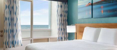 Un cuarto de hotel con una cama grande, vista al océano y un cuadro de un muelle.