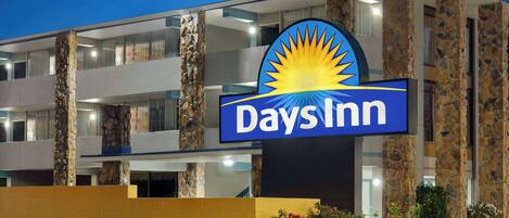 Une enseigne Days Inn avec un emblème solaire, des piliers en pierre et un mur jaune.
