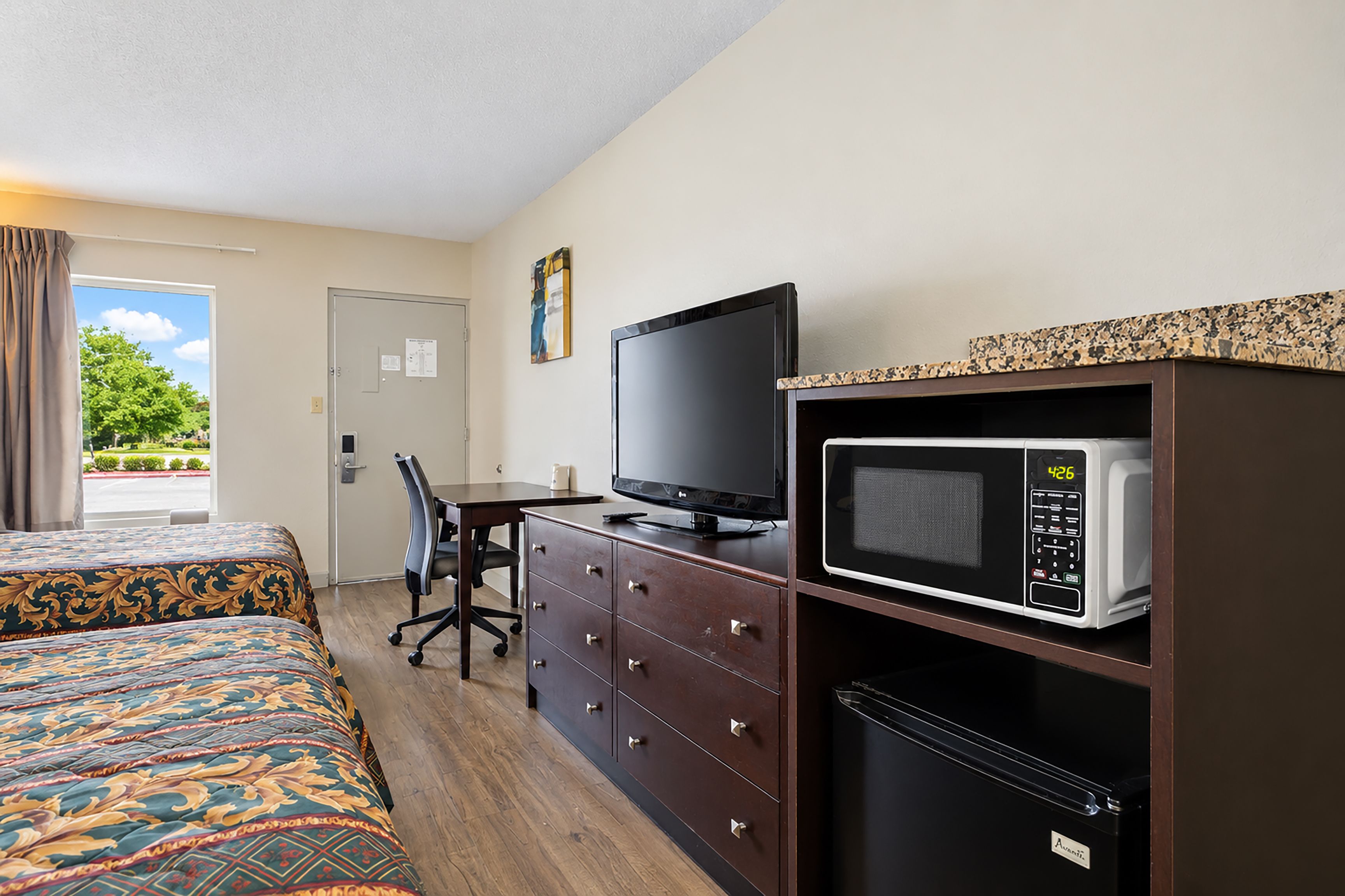 A hotel room with a bed, a desk, a television, and a microwave.