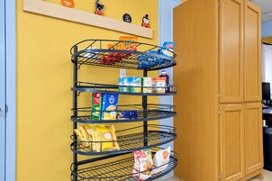 Un estante metálico de varios niveles contra una pared amarilla, con diversos alimentos y artículos del hogar.