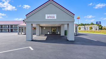 Un edificio con un cartel que dice 'OFFICE' en la entrada, un estacionamiento y un letrero de McDonald's al fondo.