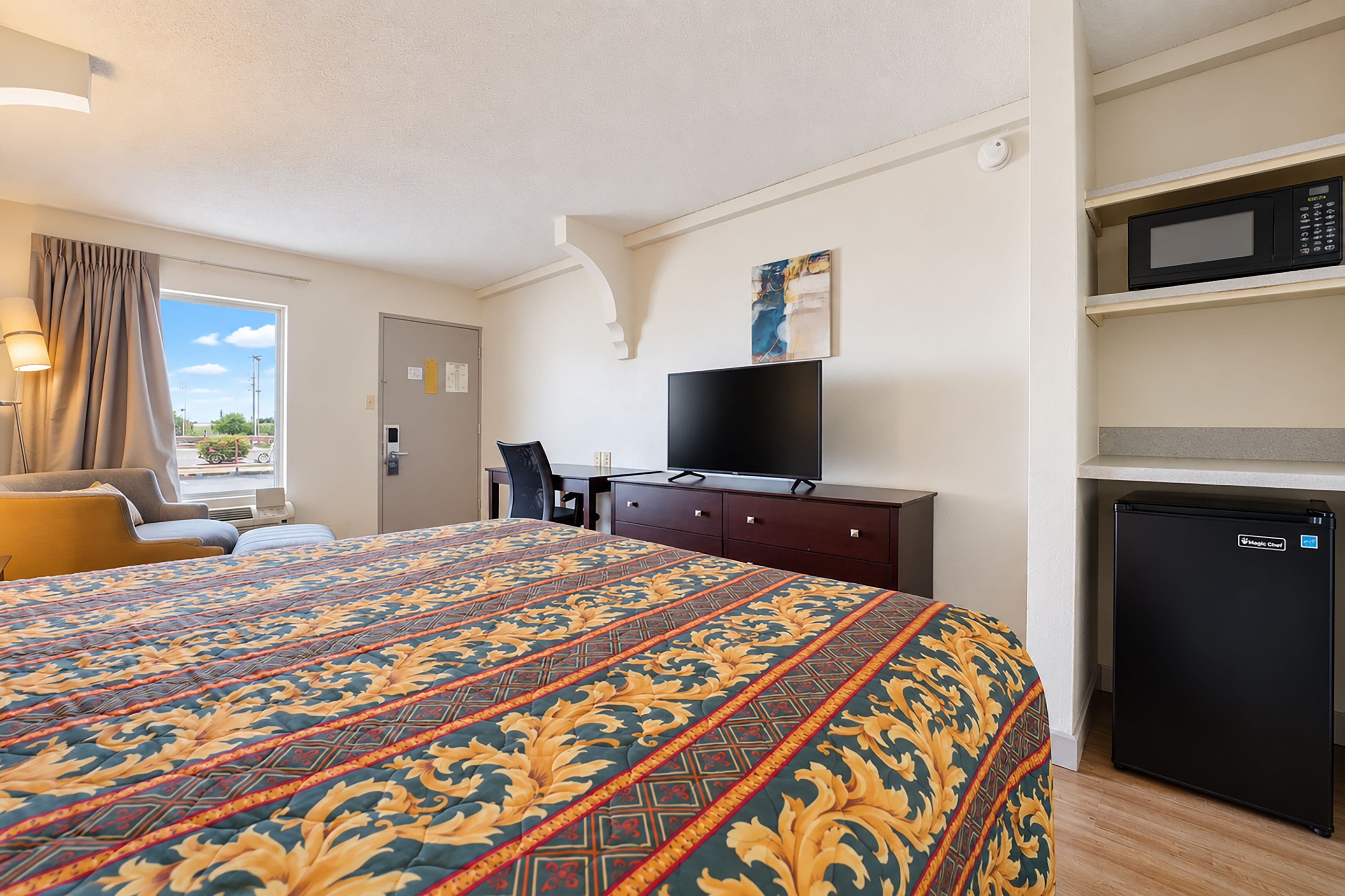 Een hotelkamer met een groot bed, een bureau, een televisie, een magnetron en een koelkast.
