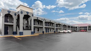 A multi-story motel with a parking lot, featuring a row of rooms with balconies and a red-roofed building in the background. - Southern Inn (Manchester)