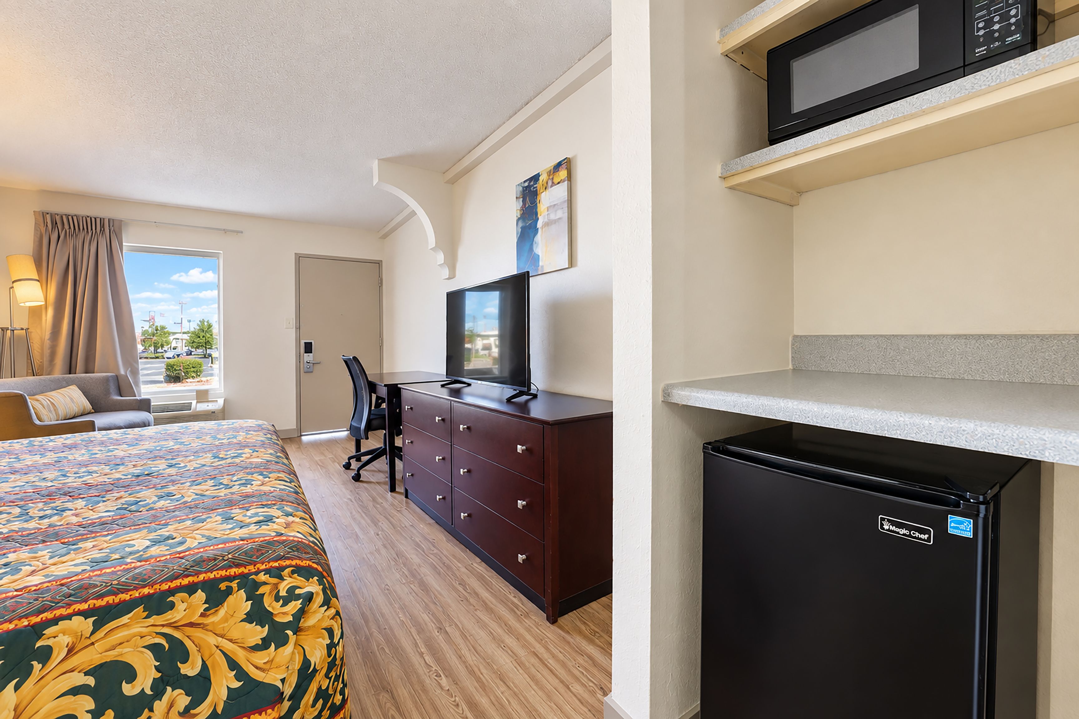 A hotel room with a bed, a desk, a chair, a television, a microwave, and a refrigerator.