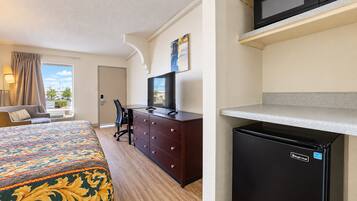 A hotel room with a bed, a desk, a chair, a television, a microwave, and a refrigerator.