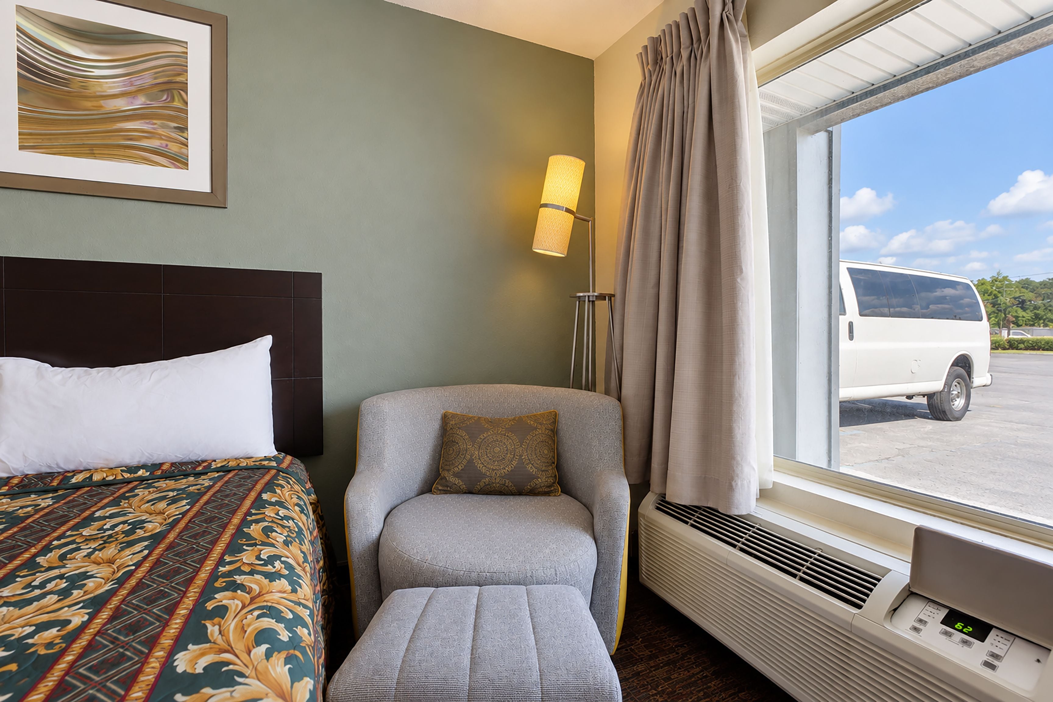 Habitación de hotel con cama, una silla, una mesita, ventana con cortinas y aire acondicionado de pared.