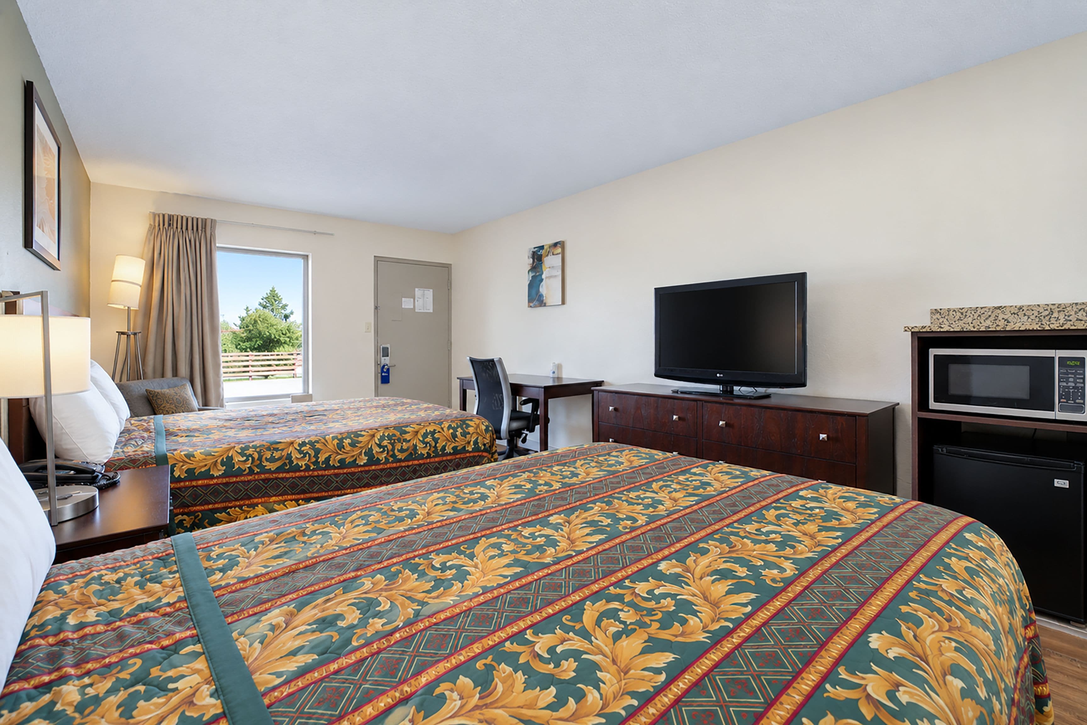Habitación de hotel con dos camas, un escritorio, un televisor, un microondas y una ventana con cortinas.