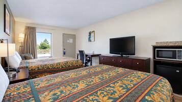 Habitación de hotel con dos camas, un escritorio, un televisor, un microondas y una ventana con cortinas.