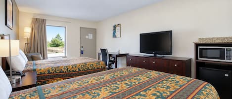 A hotel room with two beds, a desk, a television, a microwave, and a window with curtains.