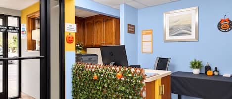 A reception area with a wooden desk, a computer, and a plant. There is a sign for WiFi password and a 'Positive Mindset' sign on the wall.