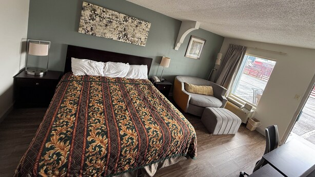 A hotel room with a large bed, a nightstand, a desk, a chair, and a window with curtains. - Southern Inn (Manchester)