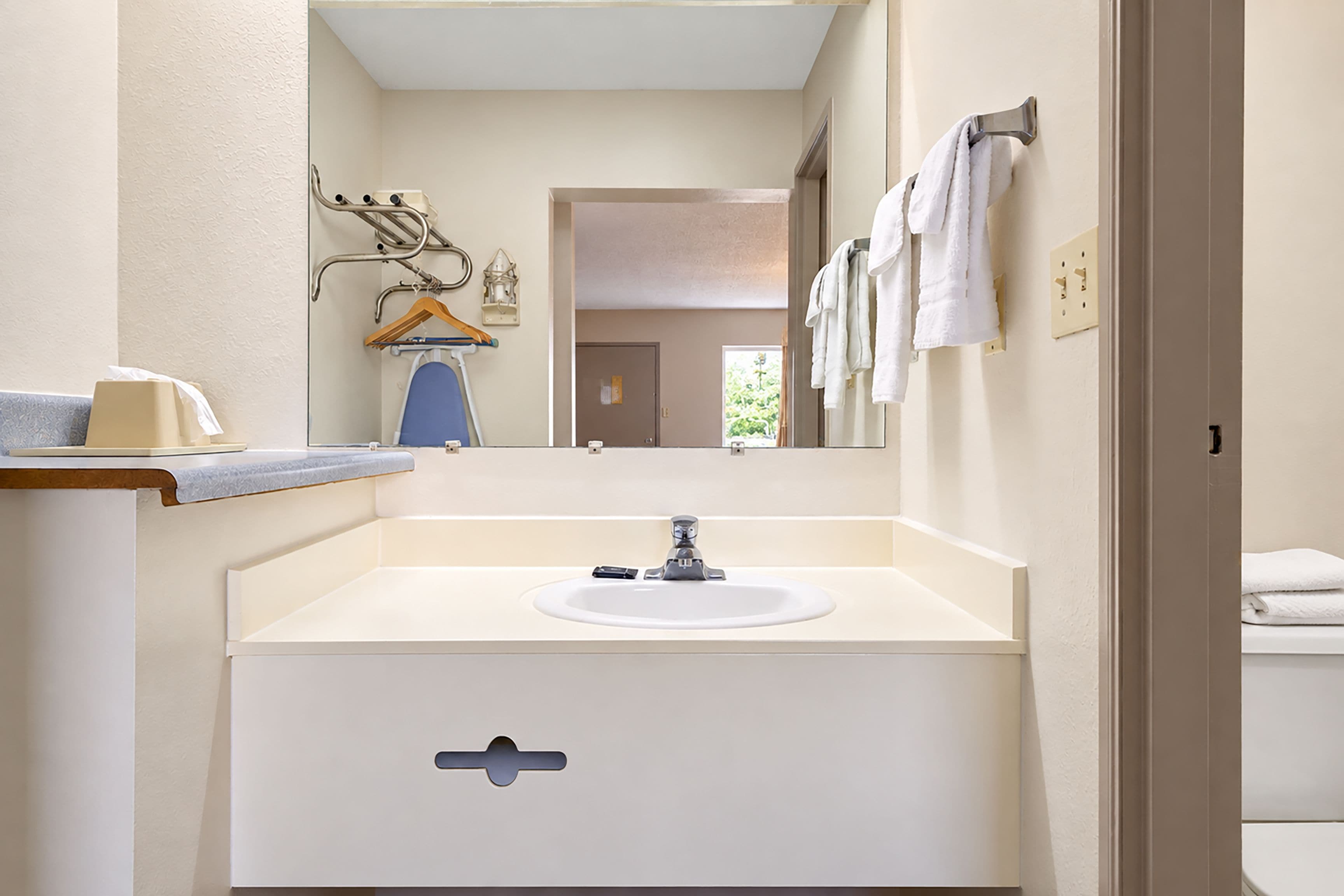 A bathroom with a sink, mirror, towel rack, and a door leading to another room.