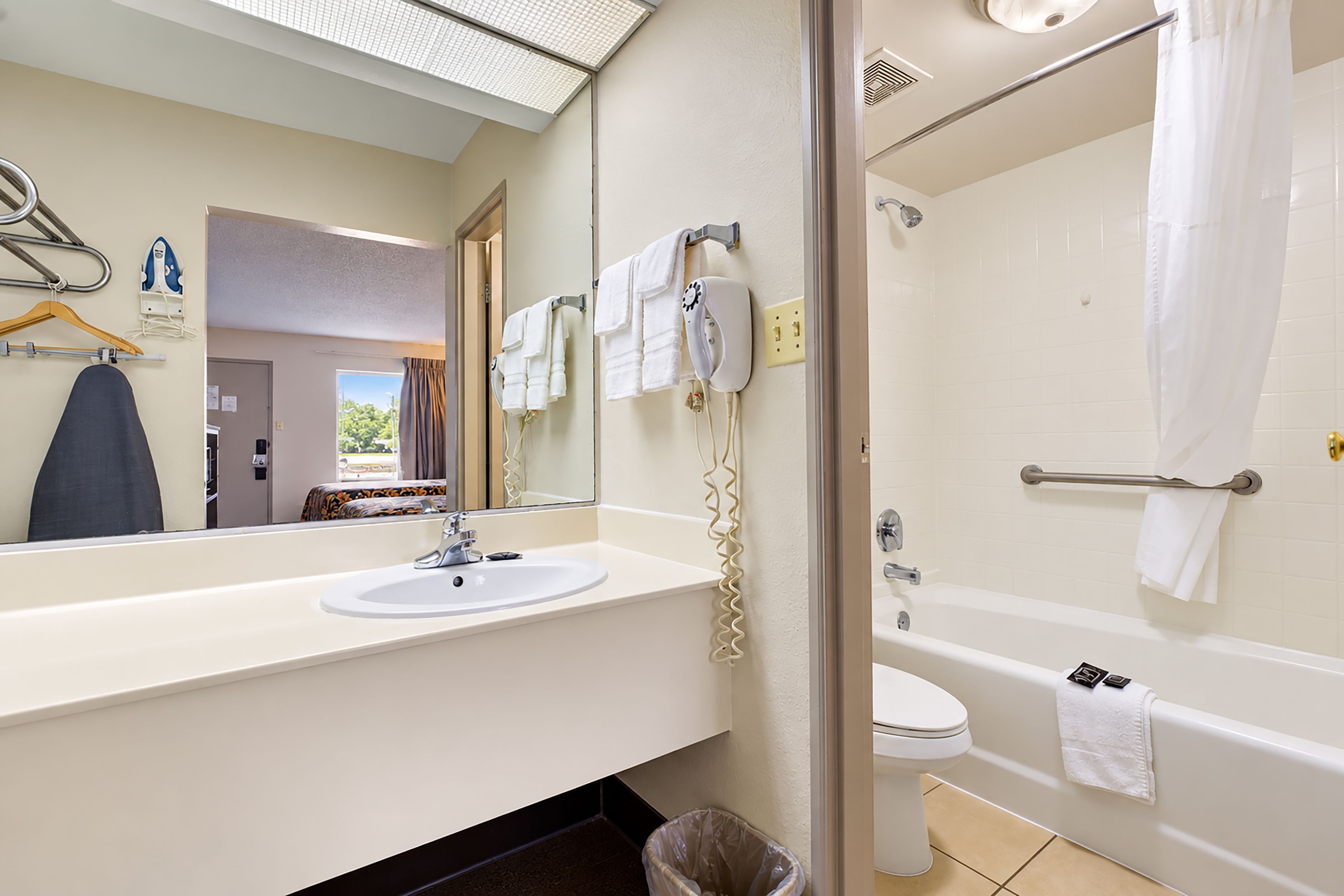 Une salle de bain d’hôtel équipée d’un lavabo, d’un miroir, d’un porte-serviettes et d’un espace douche.