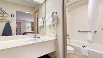 Une salle de bain d’hôtel équipée d’un lavabo, d’un miroir, d’un porte-serviettes et d’un espace douche.
