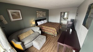 A hotel room with a sofa, two beds, a desk, and a bathroom visible through a glass door. - Southern Inn (Manchester)