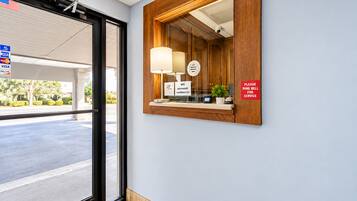 Zona de recepción de hotel con un mostrador de madera, un espejo, un cartel con la contraseña de WiFi e indicaciones para llamar al timbre para asistencia.