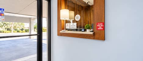 A hotel reception area with a wooden reception desk, a mirror, a sign for WiFi password, and a sign instructing to ring the bell for service.