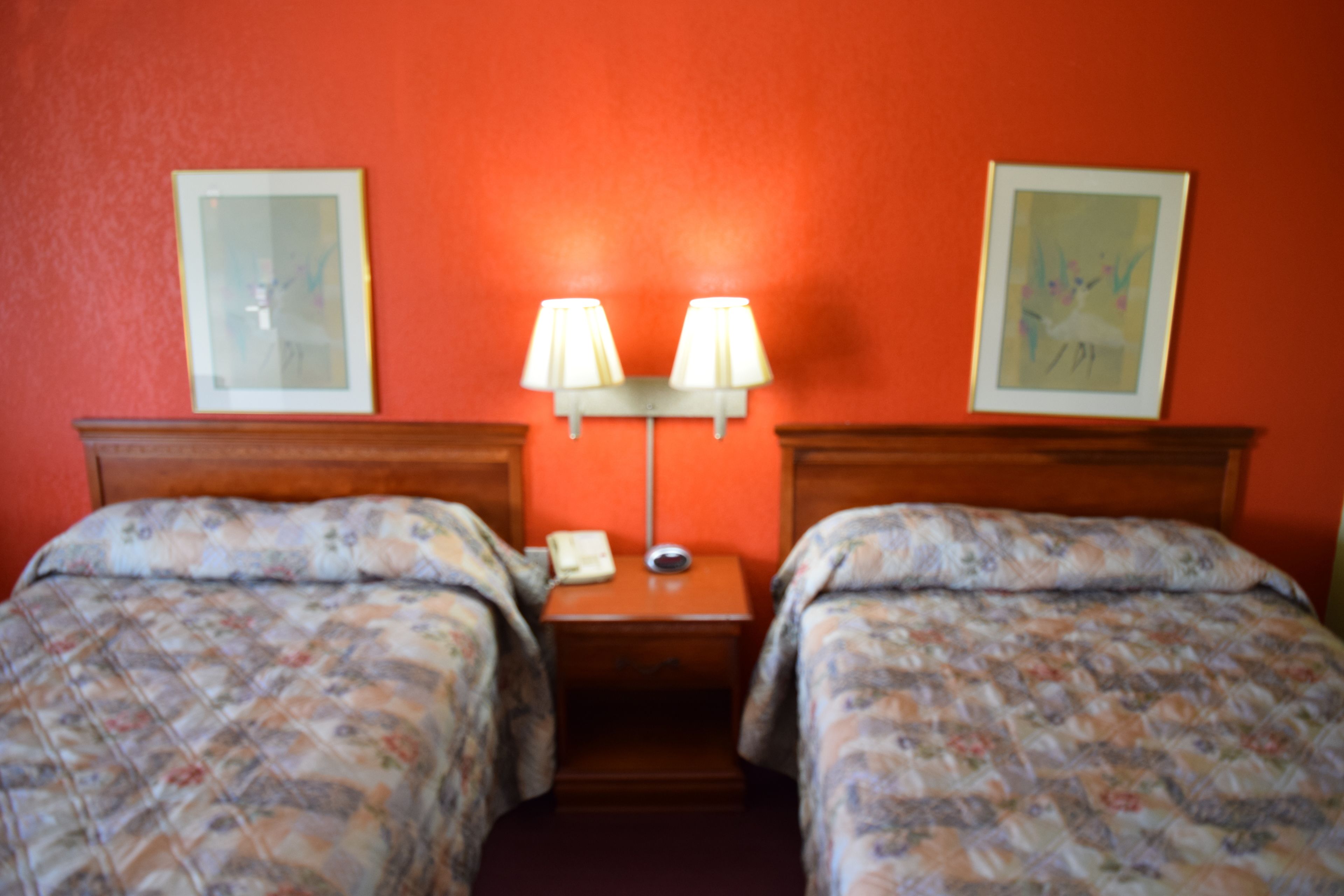 A hotel room with two beds, a nightstand, a lamp, and two framed pictures on the wall.