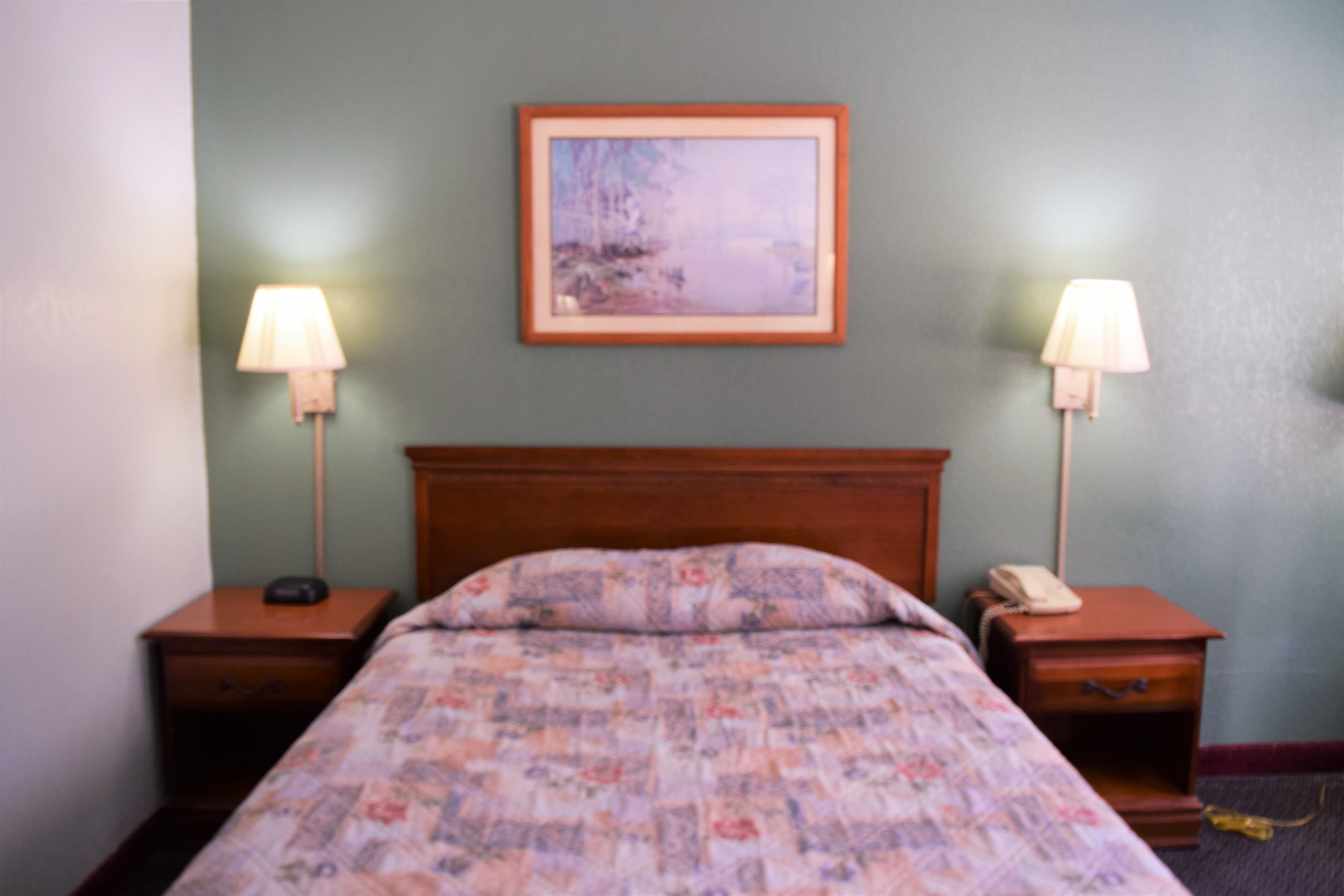 A bedroom with a wooden headboard, floral bedding, two bedside tables with lamps, and a framed picture on the wall.