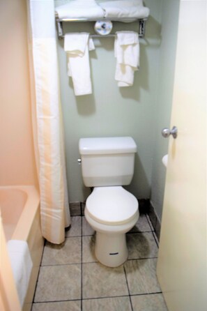 A small bathroom with a toilet, a shower curtain, and a towel rack with several towels.