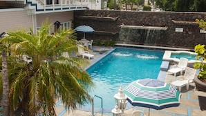 A swimming pool with lounge chairs and umbrellas, surrounded by palm trees and a stone wall. - Hotel Villa Fontana Inn (Ensenada)