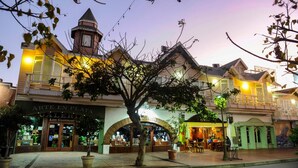 A street view at dusk with a building featuring a tower, storefronts, and outdoor seating. - Hotel Villa Fontana Inn (Ensenada)
