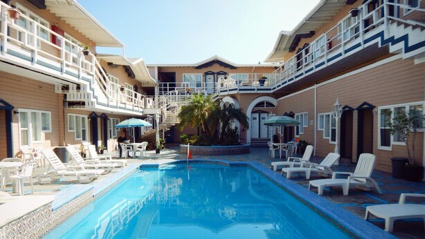 A swimming pool with lounge chairs and umbrellas, surrounded by a building with multiple balconies and a central door. - Hotel Villa Fontana Inn (Ensenada)