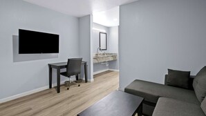 A modern living room with a grey sofa, a small table, and a TV mounted on the wall. - Americas Best Value Inn Gonzales (Gonzales)