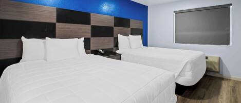 A hotel room with two beds, a blue accent wall, a large window, and a wooden floor.