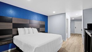 A modern hotel room with a large bed, a blue accent wall, and a wooden floor. - Americas Best Value Inn Gonzales (Gonzales)