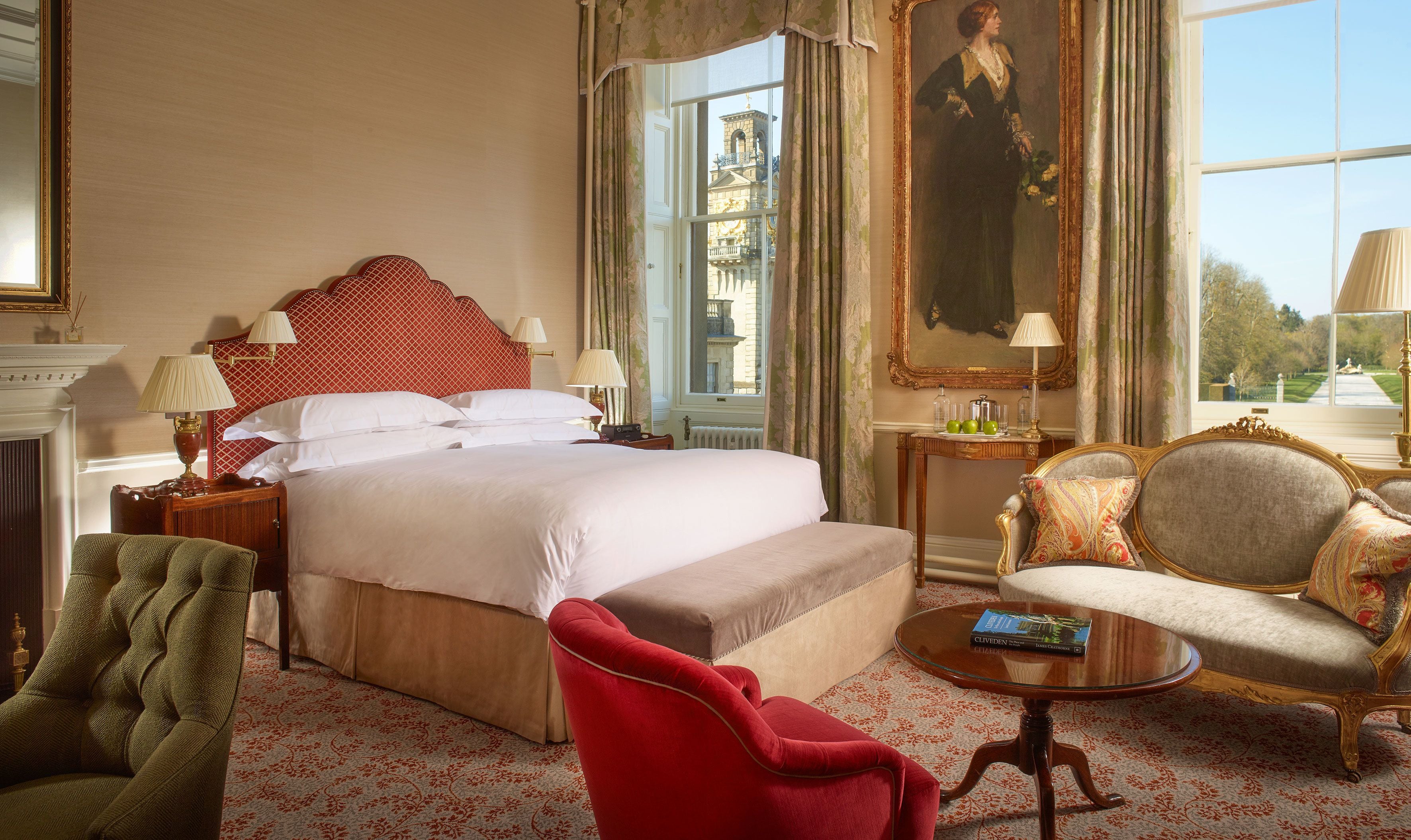 Habitación de hotel con una cama grande, zona de estar con sofá y sillón, una mesita y un cuadro en la pared.