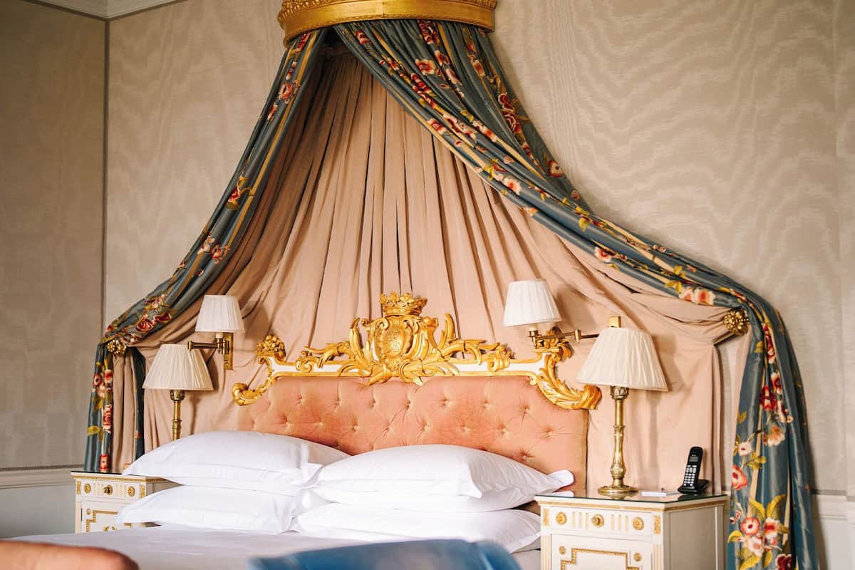 A luxurious bedroom with a tufted headboard, ornate gold detailing, and a canopy with floral patterns.