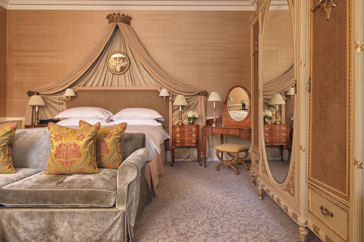 A luxurious bedroom with a large bed, a chaise lounge, a dressing table, and a large mirror.