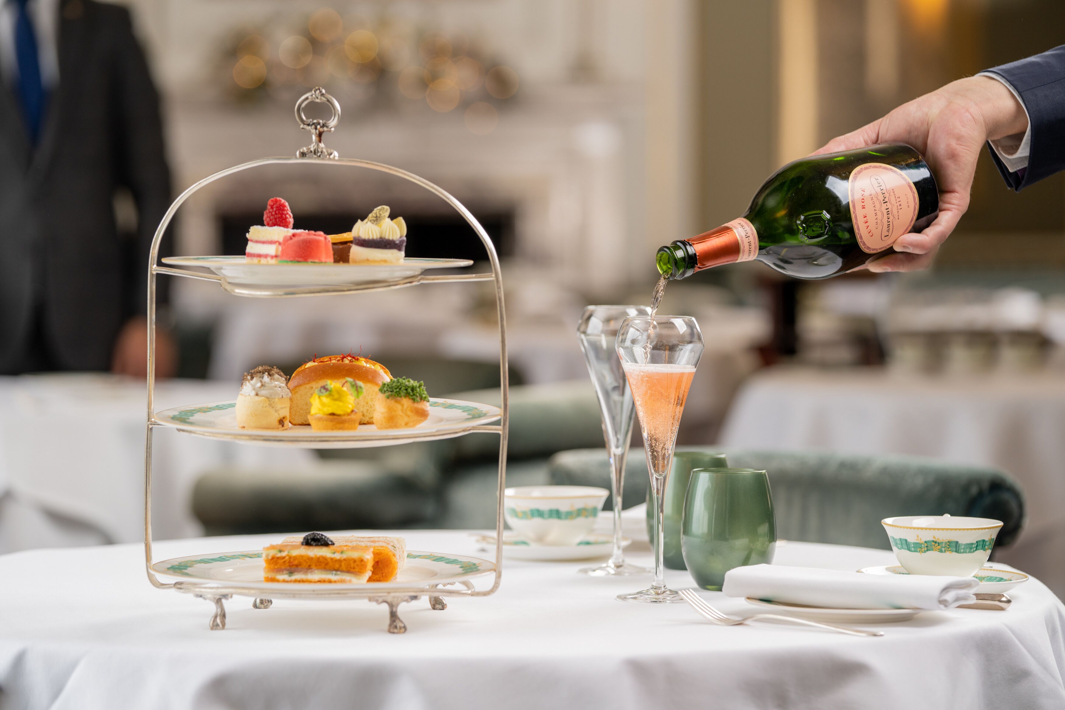 A three-tiered dessert stand with various pastries and a bottle of champagne being poured into a glass.