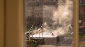 A hot tub with steam rising, surrounded by a brick wall and a building in the background.